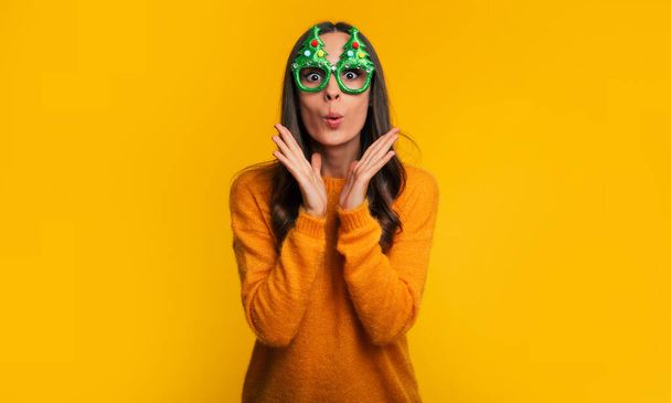 Κοντινό πλάνο φωτογραφία του χαριτωμένο ενθουσιασμένοι κομψή γυναίκα σε αστεία χριστουγεννιάτικα γυαλιά ποζάρει και διασκεδάζοντας απομονώνονται σε κίτρινο φόντο - Φωτογραφία, εικόνα