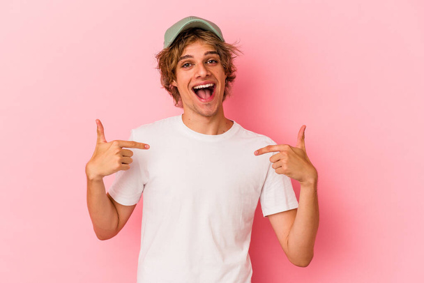 Молодий білий чоловік з макіяжем ізольований на рожевому фоні здивований вказуючи пальцем, посміхаючись широко
. - Фото, зображення