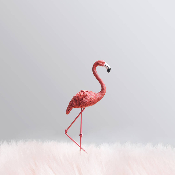 Eenzame vogel minimaal concept. Een roze flamingo die alleen staat, omringd door pluizig bont. Lichtgrijze achtergrond - Foto, afbeelding