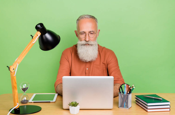 Портрет привлекательного сфокусированного седовласого человека, печатающего отчет по электронной почте, изолированный на зеленом фоне - Фото, изображение