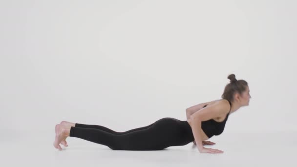 Позиция кобры. Вид сбоку снимок гибкой женщины, выполняющей упражнения на растяжку спины, практикующейся на белом фоне - Кадры, видео