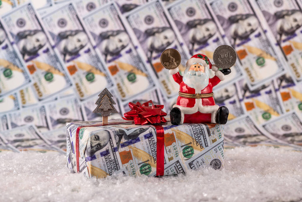 Figurine en céramique du Père Noël tenant dans une main une pièce de 1 dollar, et dans l'autre moitié d'un dollar sur fond de billets de dollar et attributs de Noël - Photo, image