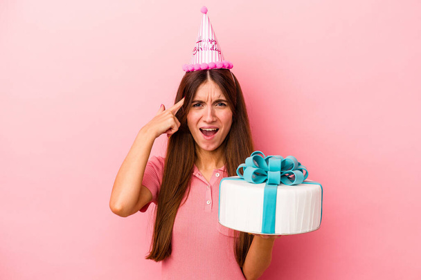 Giovane donna caucasica che celebra un compleanno isolato su sfondo rosa mostrando un gesto di delusione con l'indice. - Foto, immagini