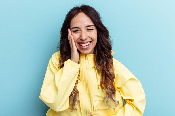 Young mexican woman isolated on blue background laughs happily and has fun keeping hands on stomach. - Photo, Image