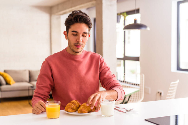 Молодой человек смешанной расы ест круассан на кухне утром - Фото, изображение