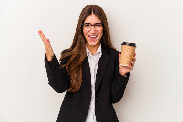 白い背景に孤立したテイクアウトコーヒーを手にした若い白人ビジネスマン女性は驚き、興奮し、手を上げる. - 写真・画像