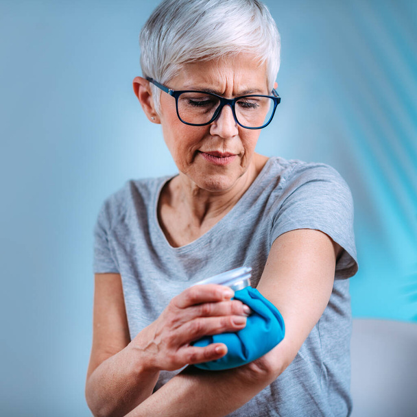 Elleboogpijn behandeling. Senior vrouw met een ijszak kompres op een pijnlijke elleboog  - Foto, afbeelding