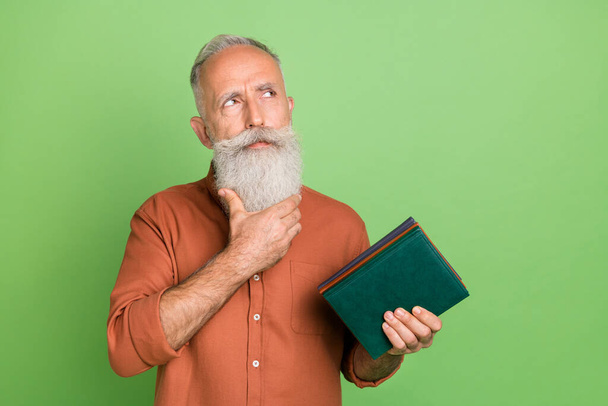 Fénykép a töprengő idős férfi figyelmes megjelenés üres tér könyv irodalom elszigetelt zöld színű háttér - Fotó, kép