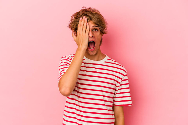 Young caucasian man with make up isolated on pink background having fun covering half of face with palm. - Foto, Imagem
