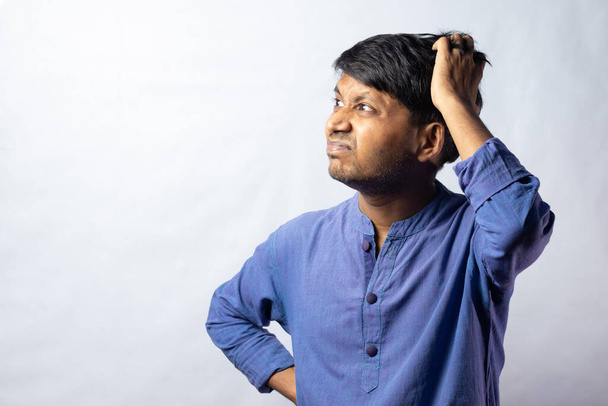 A young Indian male in blue dress scratching head and thinking on white background - Photo, Image