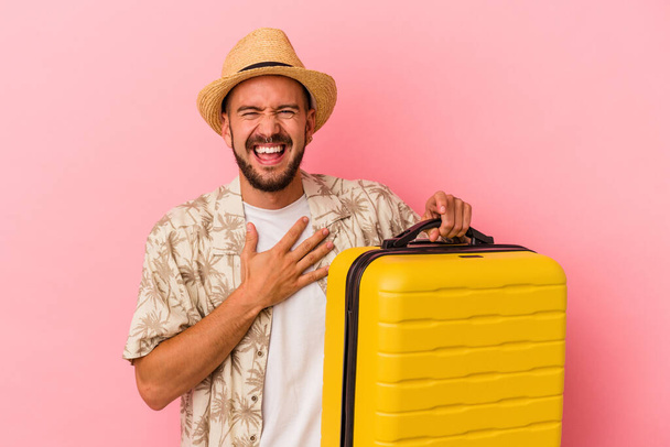 Young caucasian man with tattoos going to travel isolated on pink background  laughs out loudly keeping hand on chest. - Photo, Image