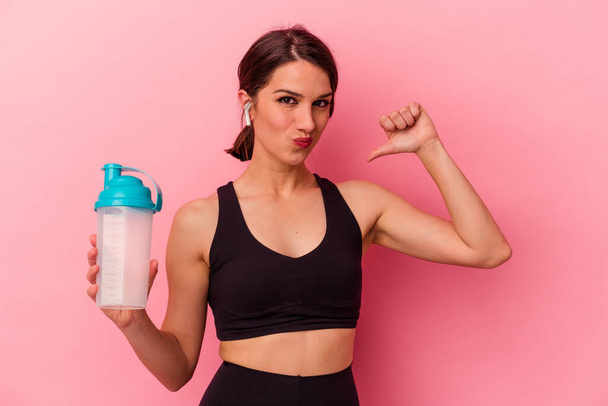 Young caucasian woman drinking a protein shake isolated on pink background feels proud and self confident, example to follow. - Fotó, kép