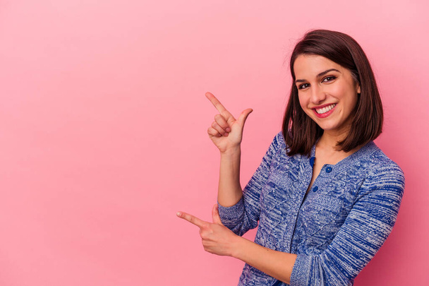 Mulher caucasiana jovem isolado no fundo rosa apontando com os dedos indicador para um espaço de cópia, expressando emoção e desejo. - Foto, Imagem