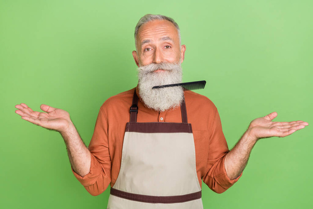 Photo of mature man hairdresser brush stack in beard clueless puzzled isolated over green color background - Foto, Bild