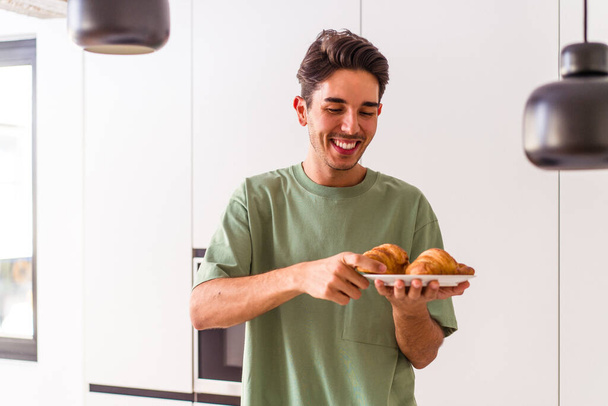 młody mieszane rasa człowiek jedzenie croissant w kuchnia w w w rano - Zdjęcie, obraz