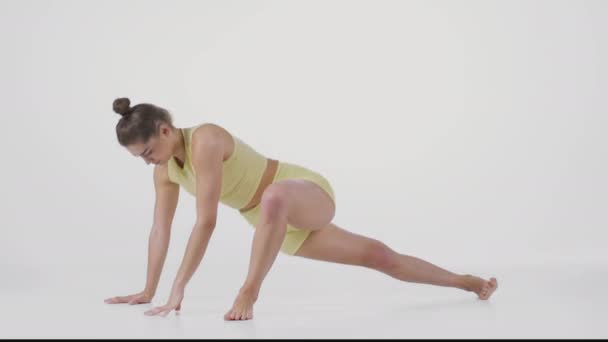 Joven deportista flexible dama haciendo Downward Dog y Matsyendrasana posa, estirando su cuerpo, fondo blanco - Metraje, vídeo