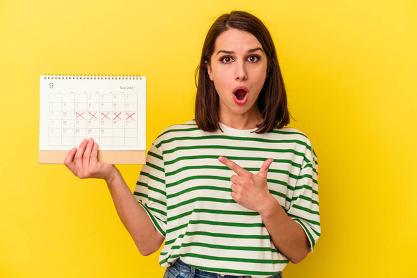 Junge Australierin mit einem Kalender auf gelbem Hintergrund, der zur Seite zeigt - Foto, Bild