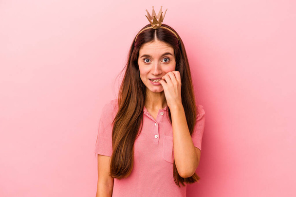 Jonge blanke vrouw draagt kroon geïsoleerd op roze achtergrond bijtende nagels, nerveus en zeer angstig. - Foto, afbeelding