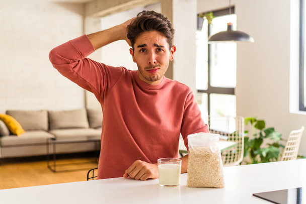 Young mixed race man eating oatmeal and milk for breakfast in his kitchen being shocked, she has remembered important meeting. - Fotoğraf, Görsel