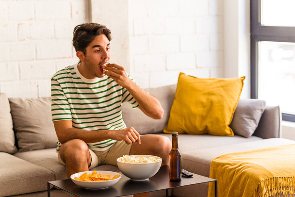 Young mixed race man eating popcorn sitting on the sofa - Photo, Image