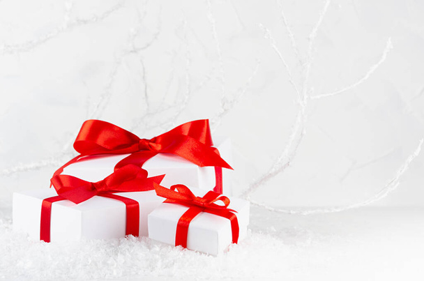 Festive three christmas gift boxes with red ribbon and bow in decorative snowdrift in fairy soft light winter forest with white frosty branches, copy space. Merry holiday New Year background. - 写真・画像