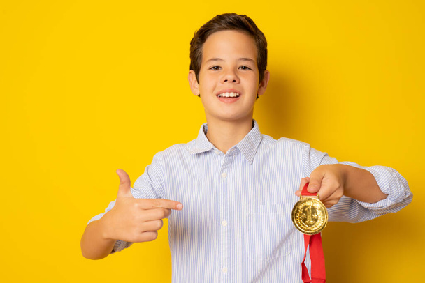 かわいい子供男の子ショー彼の金メダル孤立上の黄色の背景. - 写真・画像