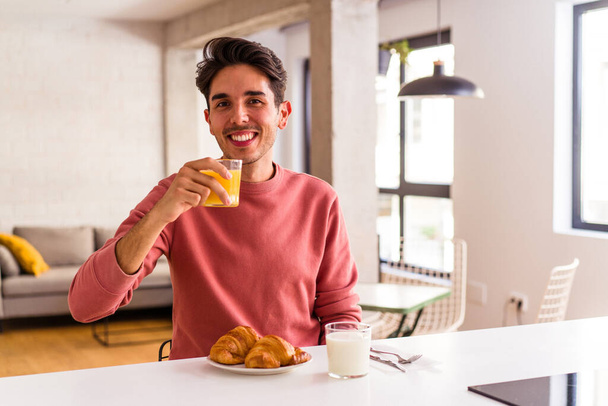 Genç melez adam sabahları mutfakta kruvasan yiyor. - Fotoğraf, Görsel