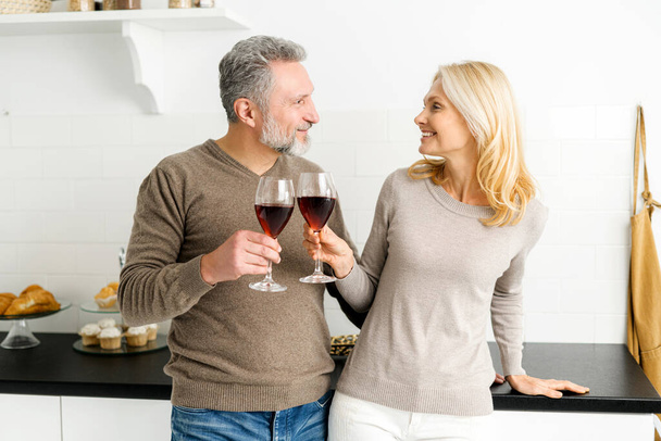 Romantic senior couple standing in the kitchen with glasses of red wine - Foto, immagini