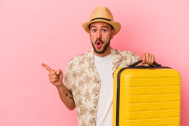 Young caucasian man with tattoos going to travel isolated on pink background  pointing to the side - Photo, Image
