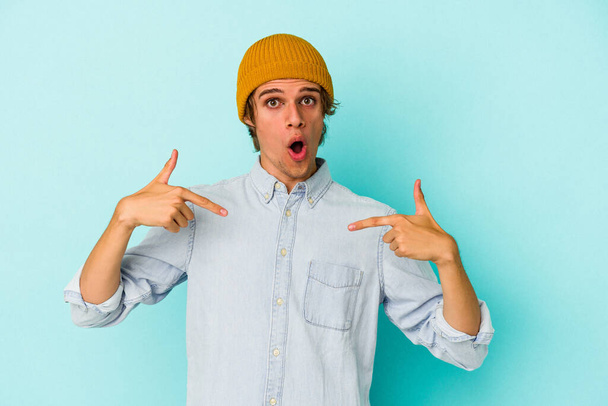 Young caucasian man with make up isolated on blue background  points down with fingers, positive feeling. - Foto, Imagem