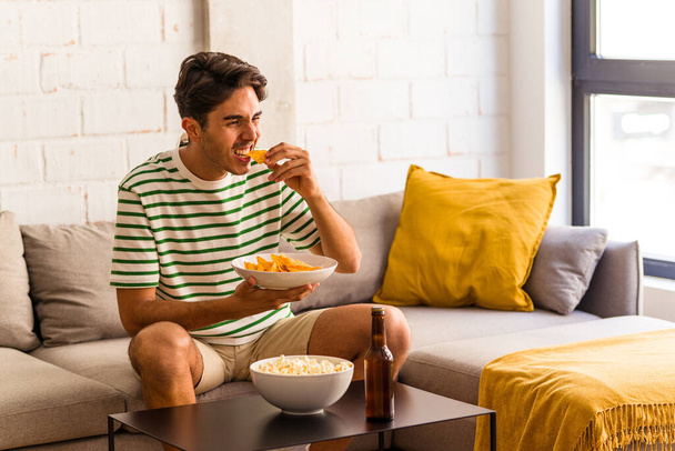 Mladý smíšený rasy muž jíst popcorn sedí na pohovce - Fotografie, Obrázek