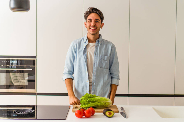 Young mixed race man preparing a salad for lunch happy, smiling and cheerful. - Photo, Image