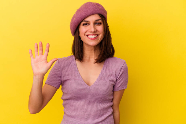 Sarı arka planda izole edilmiş genç beyaz kadın gülümseyerek beş numarayı parmaklarıyla gösteriyor.. - Fotoğraf, Görsel