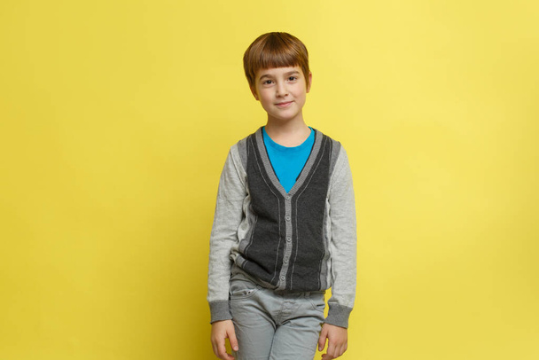 A cute smiling boy in casual stylish clothes stands isolated on a yellow background. - Photo, image
