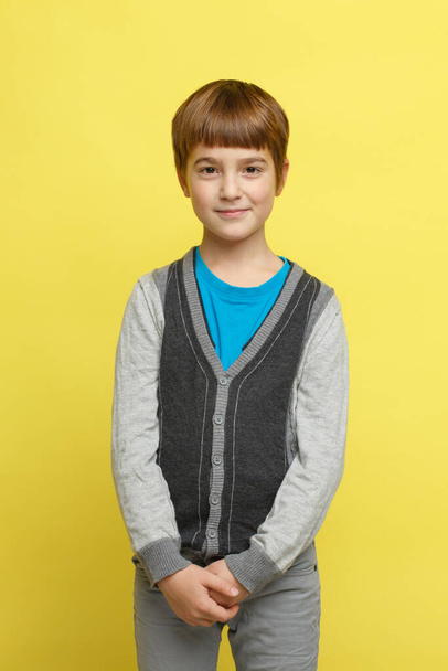 A cute smiling boy in casual stylish clothes stands isolated on a yellow background. - Фото, изображение