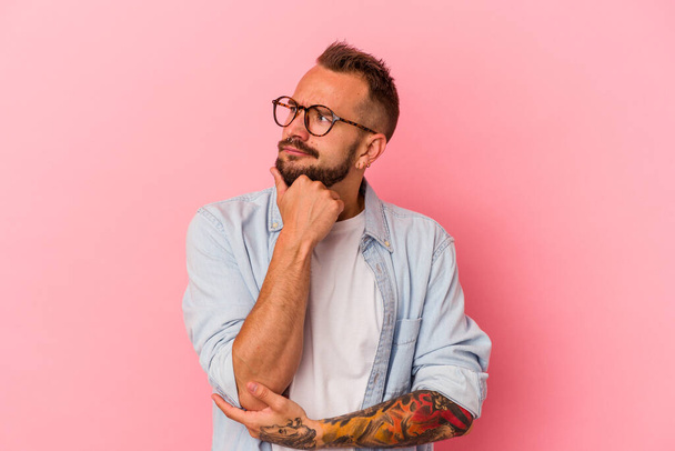 Young caucasian man with tattoos isolated on pink background  thinking and looking up, being reflective, contemplating, having a fantasy. - Photo, image