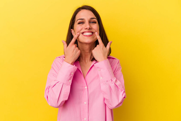 Young caucasian woman isolated on yellow background smiles, pointing fingers at mouth. - Photo, Image