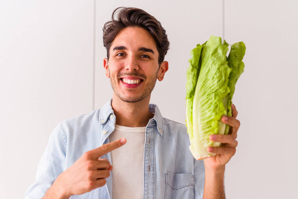 Young mixed race man holding lettuce in his kitchen - Photo, image