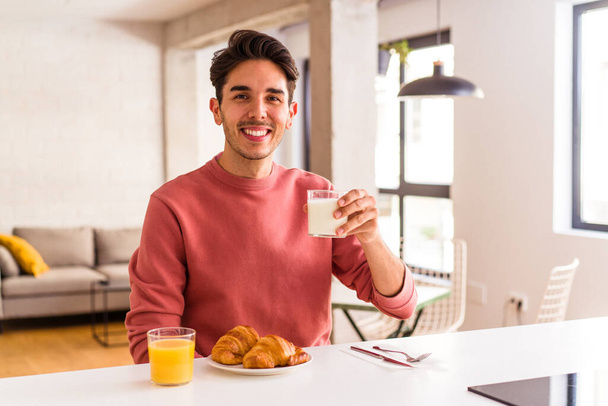 Fiatal vegyes fajú férfi eszik croissant a konyhában reggel - Fotó, kép