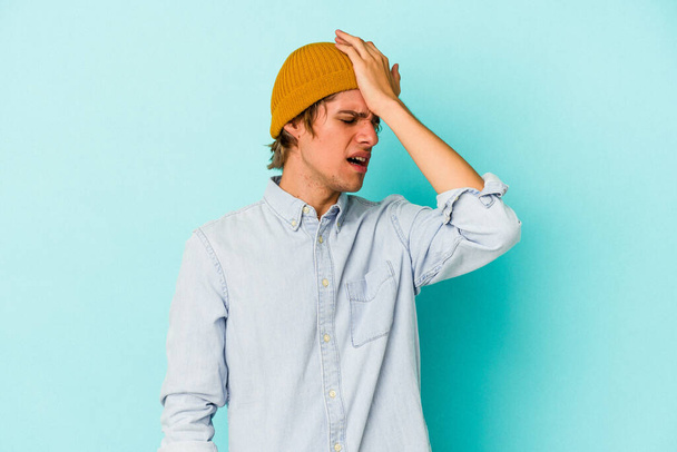 Young caucasian man with make up isolated on blue background  forgetting something, slapping forehead with palm and closing eyes. - Photo, Image