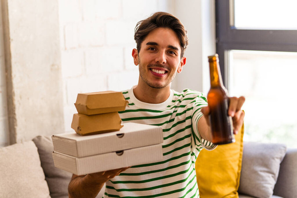 Young mixed race man eating pizza and burger and drinking beers - Foto, afbeelding
