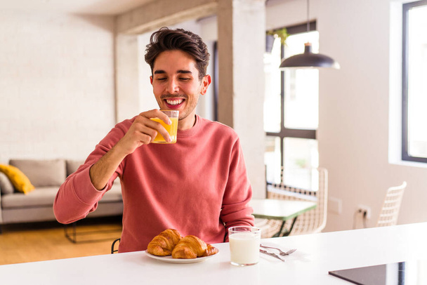 Jeune homme métis mangeant croissant dans une cuisine le matin - Photo, image