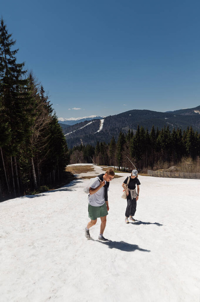 Pár turistů v letním neformálním oblečení chodí po zasněžených jarních horách, šplhají nahoru a komunikují s úsměvem na tvářích, vertikálně. - Fotografie, Obrázek
