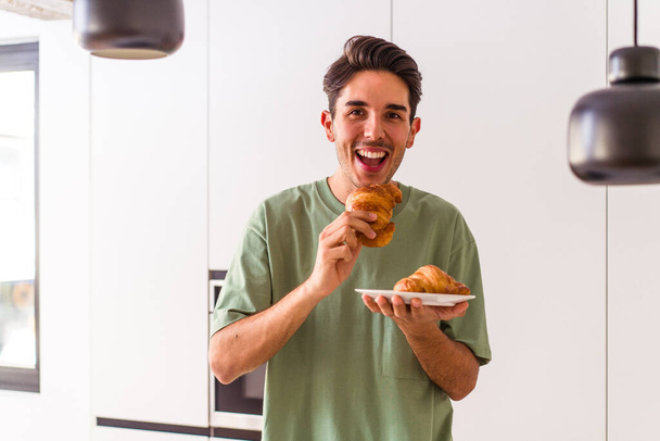Молодий змішаний чоловік їсть круасан на кухні вранці
 - Фото, зображення