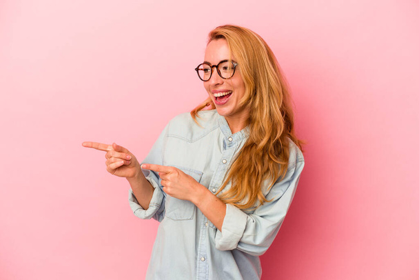 Caucasian blonde woman isolated on pink background points with thumb finger away, laughing and carefree. - Photo, Image