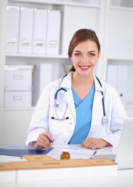 Όμορφη νεαρή χαμογελαστή γυναίκα γιατρός κάθεται στο γραφείο και w - Φωτογραφία, εικόνα