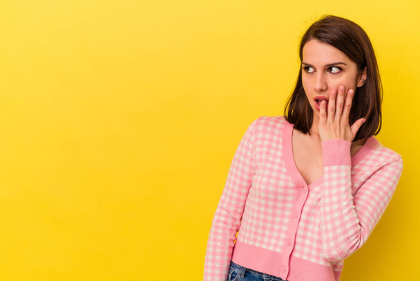 Young caucasian woman isolated on yellow background being shocked because of something she has seen. - Foto, imagen