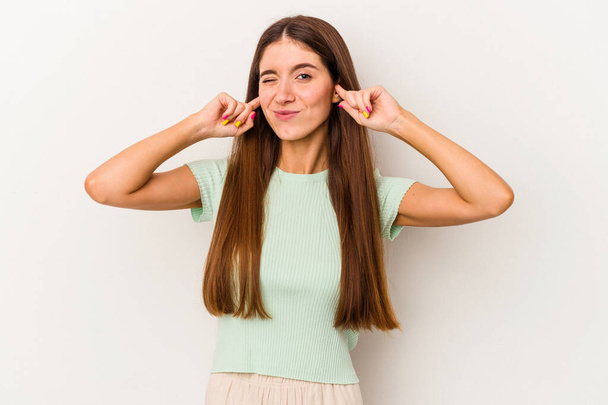 Young caucasian woman isolated on white background covering ears with fingers, stressed and desperate by a loudly ambient. - Photo, Image