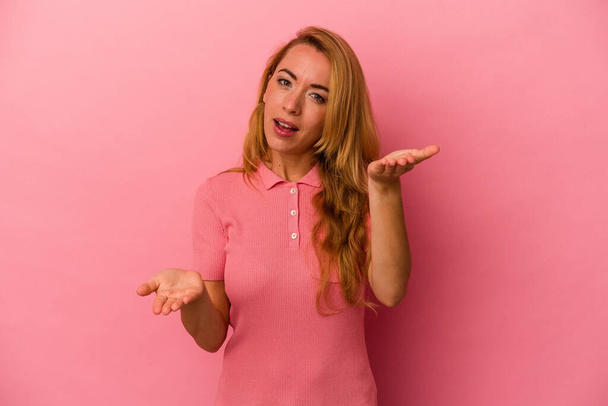 Caucasian blonde woman isolated on pink background makes scale with arms, feels happy and confident. - Φωτογραφία, εικόνα