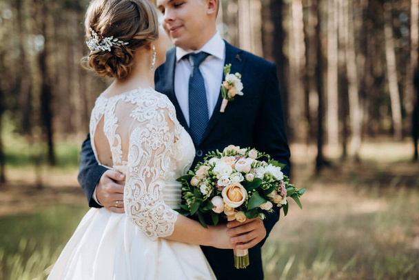 the bride and groom are walking in a pine forest on a bright day - Фото, изображение
